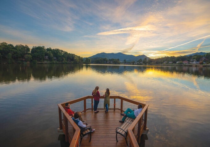 Group of people standing on a deck overlooking Lake Junaluska at sunset.