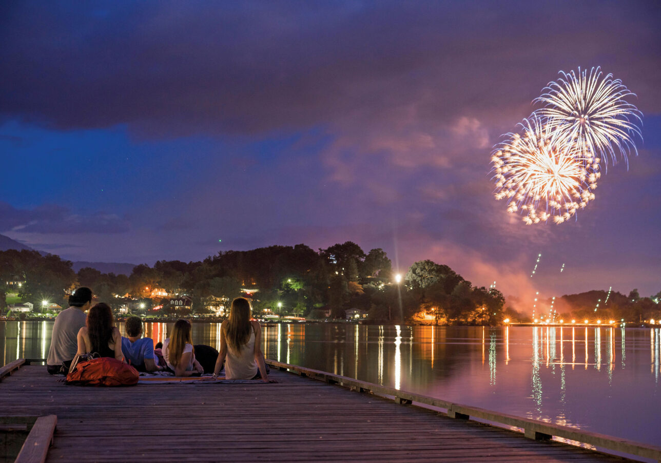 A family watching fireworks over Lake Junaluska while sitting on a wooden dock