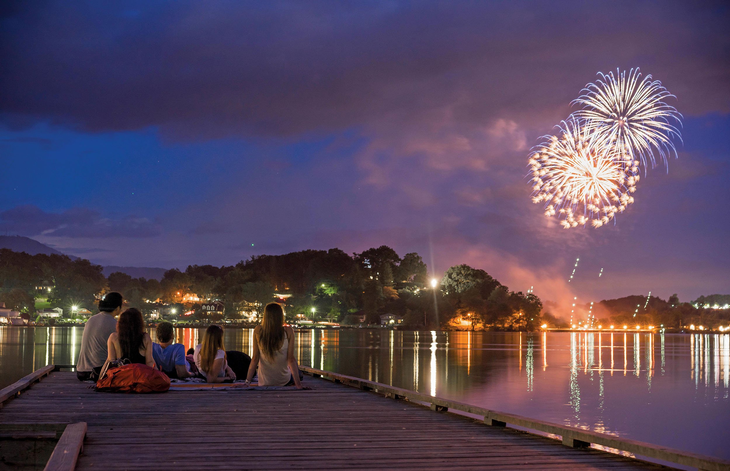 A family watching fireworks over Lake Junaluska while sitting on a wooden dock