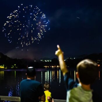 Boy points at fireworks over the lake