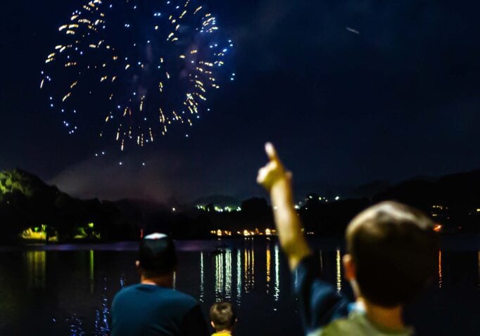 Boy points at fireworks over the lake